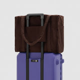 Brown bag with a handle on top of a purple suitcase against a white background