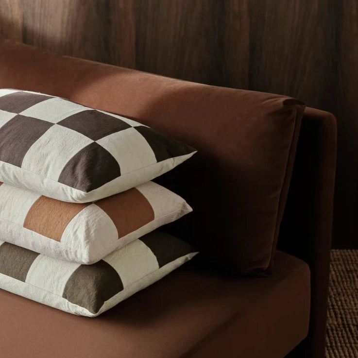 Fold Patchwork Cushion, Olive by ferm LIVING, on a brown sofa