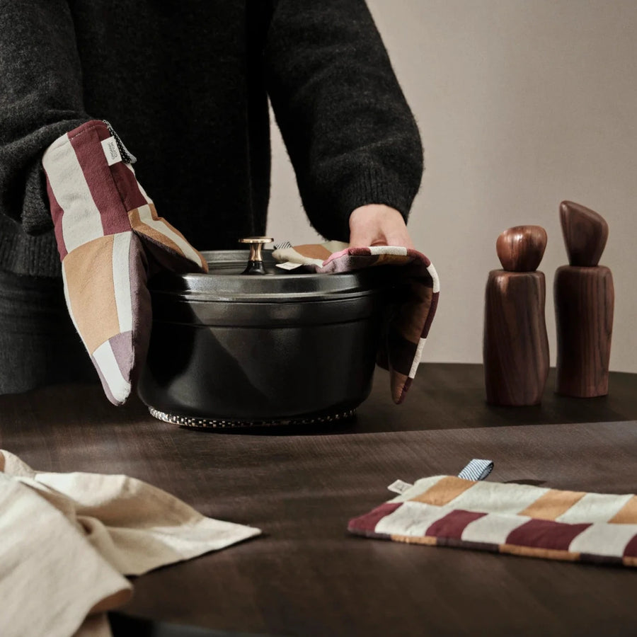 Person lifting a dark pot with a patchwork oven glove in a kitchen