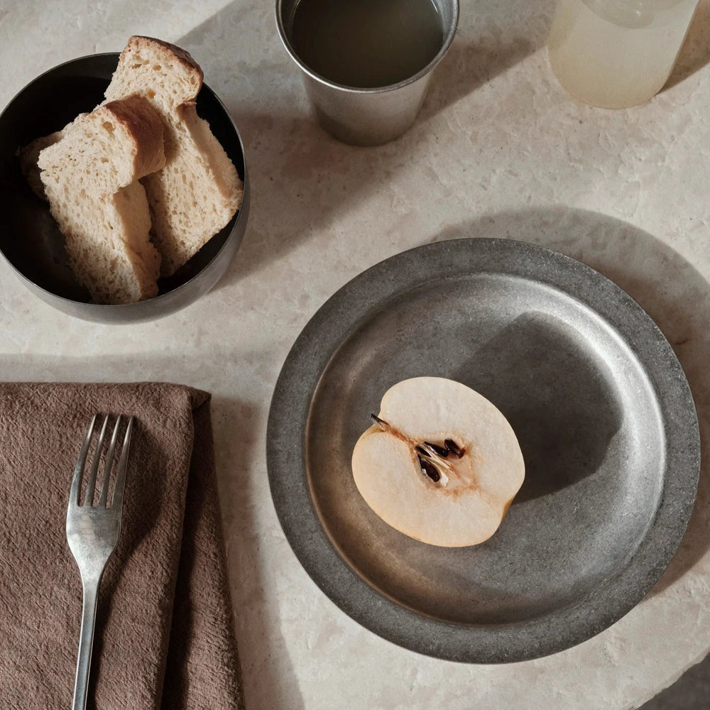 Tumbled Plate, Stainless Steel by ferm LIVING, with an apple slice on a table