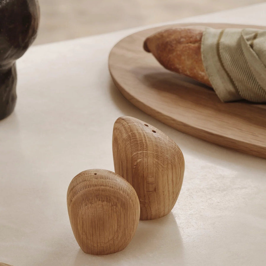 Cairn Salt and Pepper Shakers, Set of 2, Light Wood by ferm LIVING, beside bread on a white table