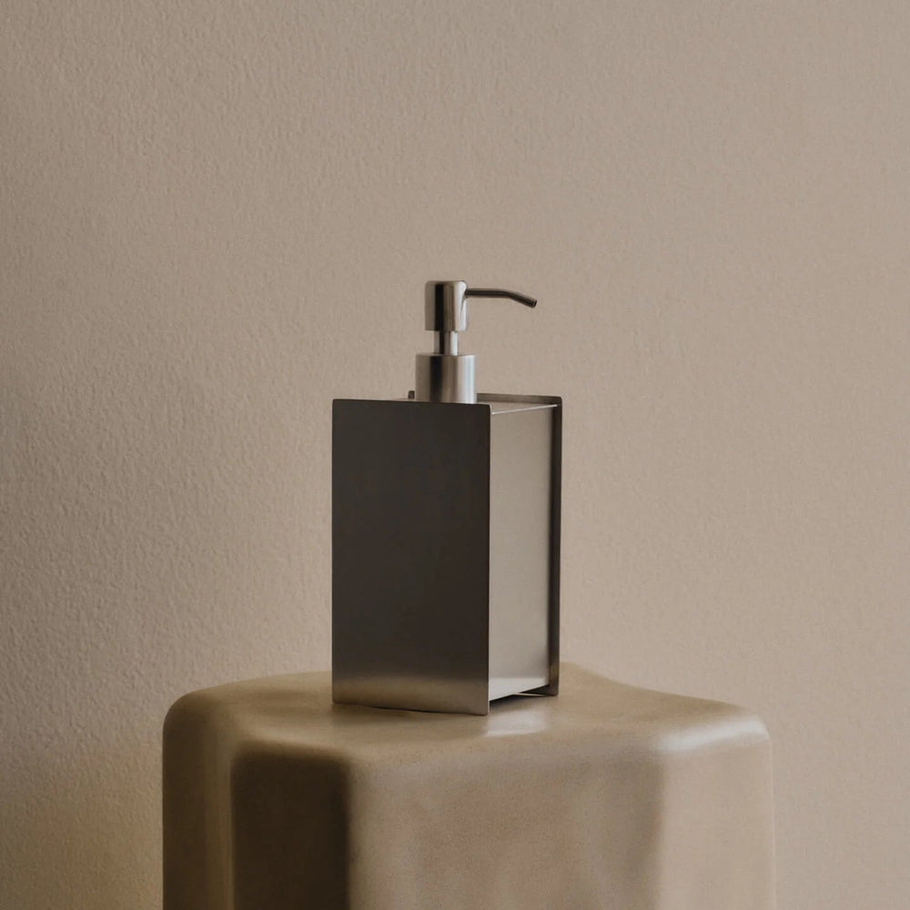 Sama Soap Dispenser, Brushed Stainless Steel by ferm LIVING, on a stone plinth