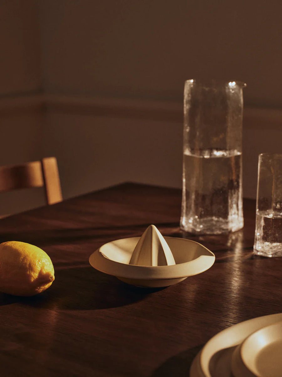 Erena Citrus Juicer, Cream by ferm LIVING, on a dark table with a lemon