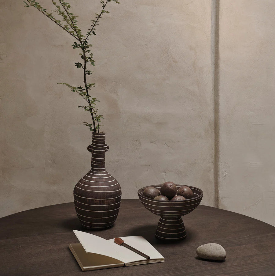 Brura Bowl, Coffee/White by ferm LIVING, with a vase of stems on a dark table