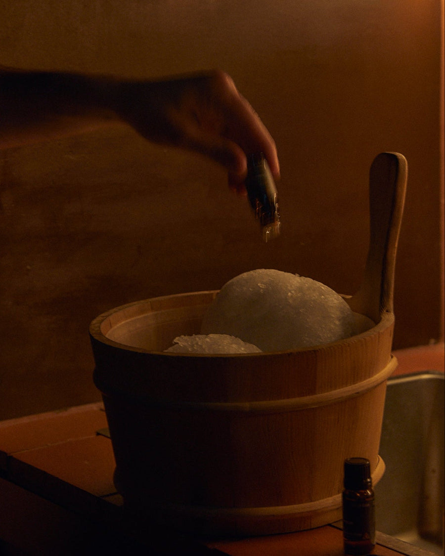 Shinrin-Yoku Essential Oil Blend, 10ml by Earl of East, being added to a wooden bath bucket