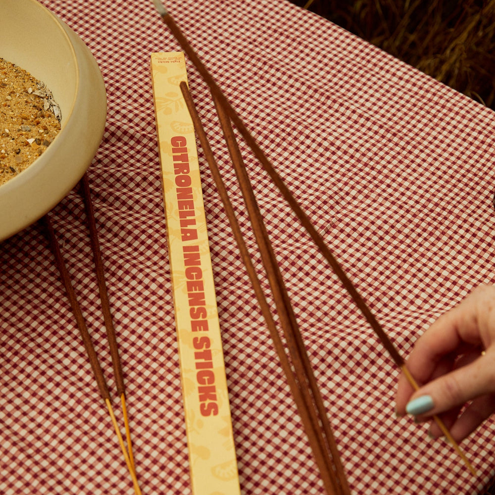 Hands holding Earl of East Citronella incense over a check tablecloth