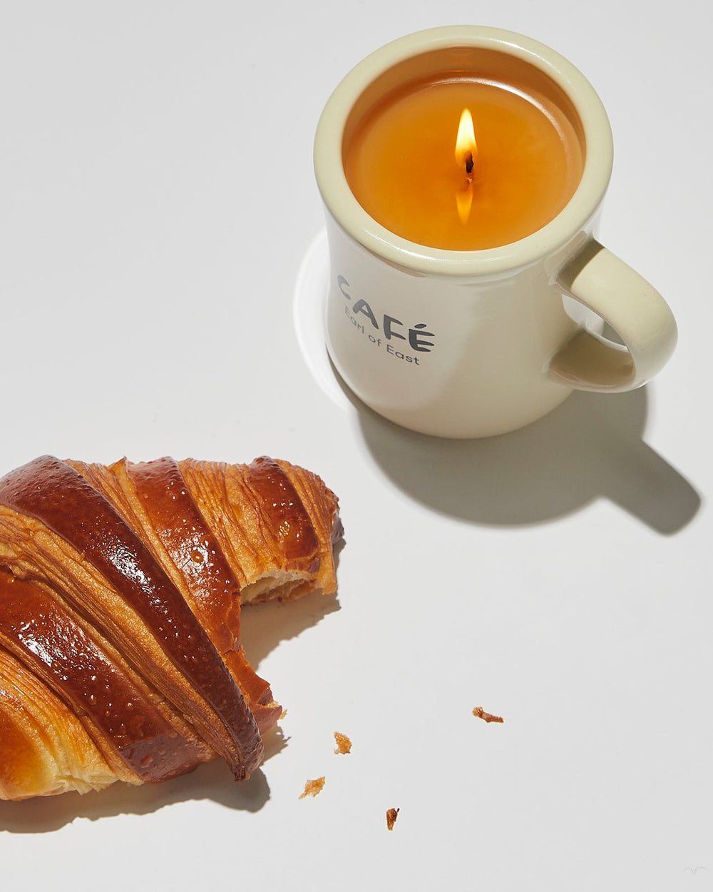 Croissant Scented Candle in Mug, 300ml by Earl of East, lit beside a croissant