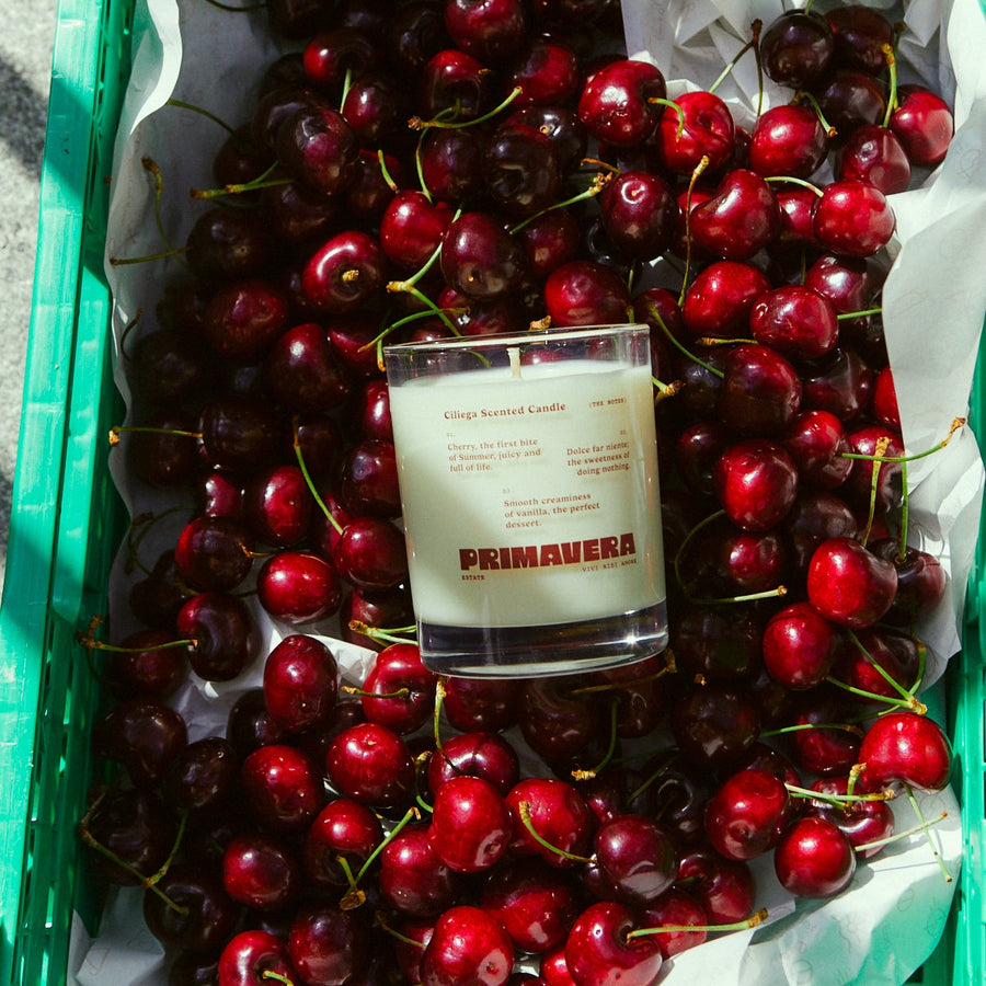 Ciliegia Scented Candle, 250ml by Earl of East, lit among fresh cherries