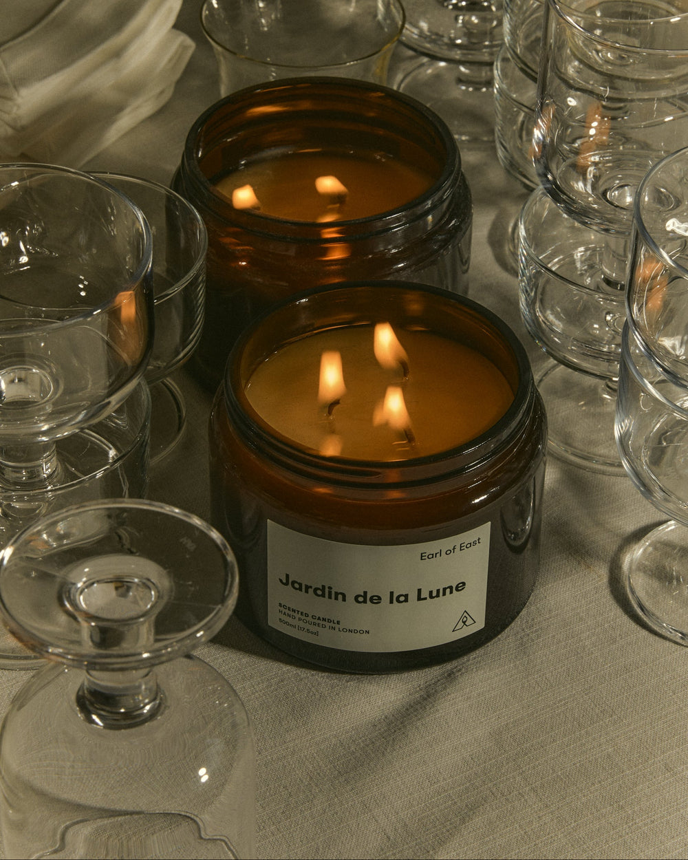 Jardin de la Lune Large Scented Candle, 500ml by Earl of East, lit among glassware in candlelight