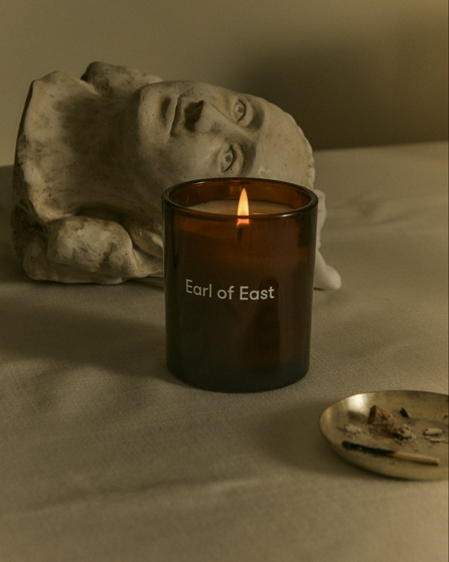 Jardin de la Lune Scented Candle, 260ml by Earl of East, lit beside a stone bust