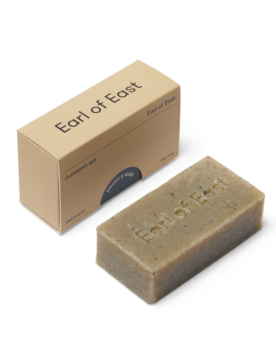 A beige-colored cleansing soap bar with 'Earl of East' engraved on it, accompanied by its packaging