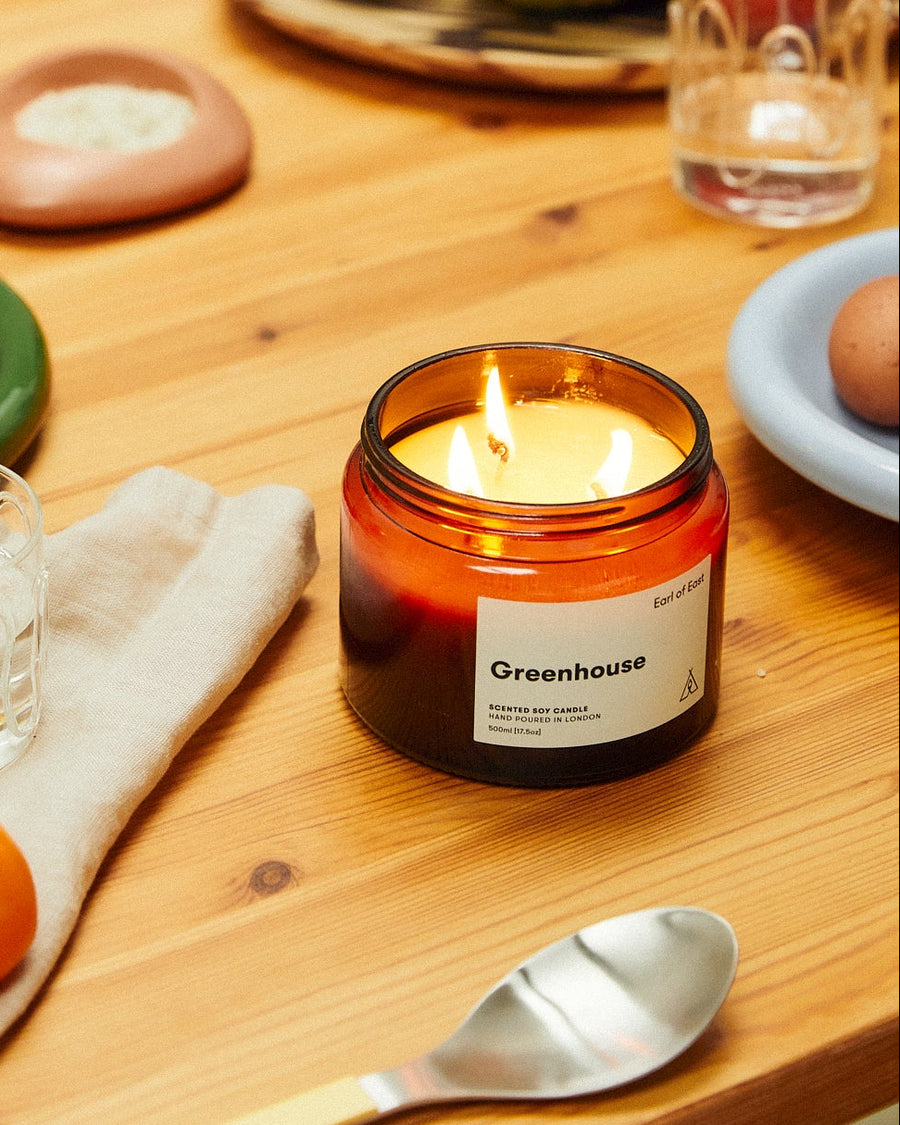 Greenhouse Large Scented Candle, 500ml by Earl of East, lit on a wooden table with fruit
