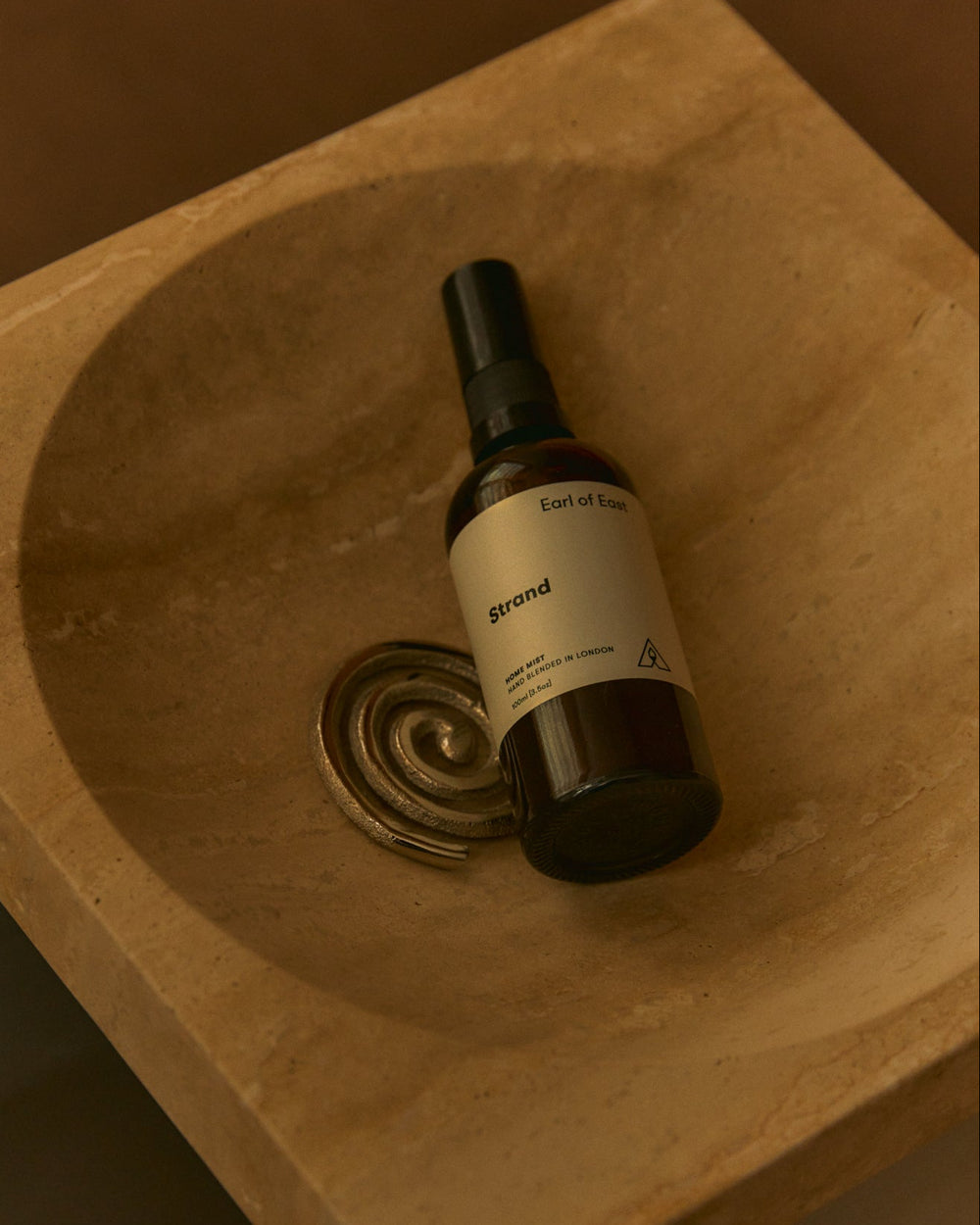 A Strand Home Mist resting in a carved stone basin.