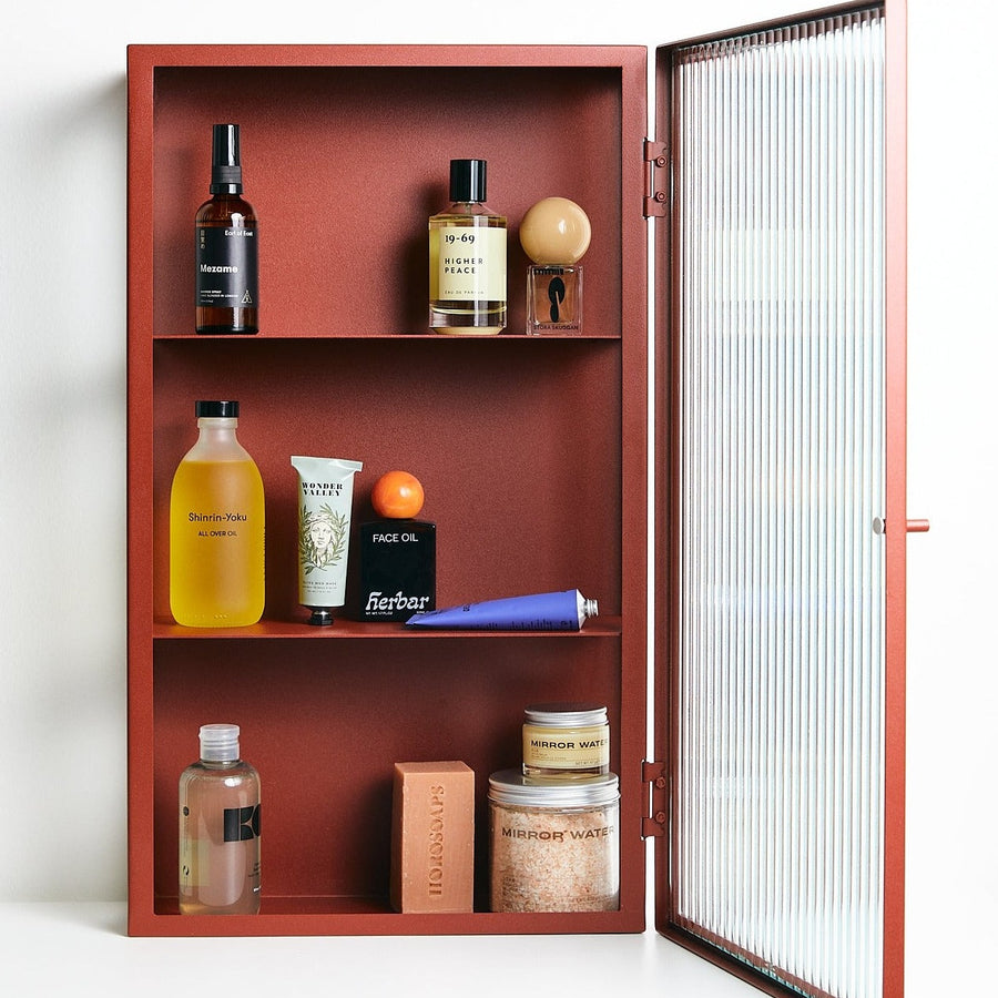 Haze Wall Cabinet, Reeded Glass, Oxide Red by ferm LIVING, door open holding bathroom products