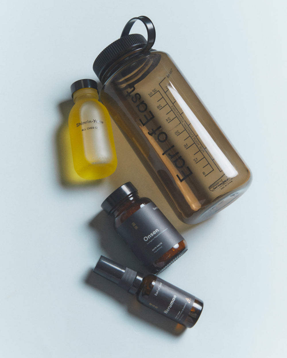 A styled flat-lay of wellness products on a light gray background, featuring a translucent brown water bottle, a small yellow bottle, and two dark amber supplement bottles.