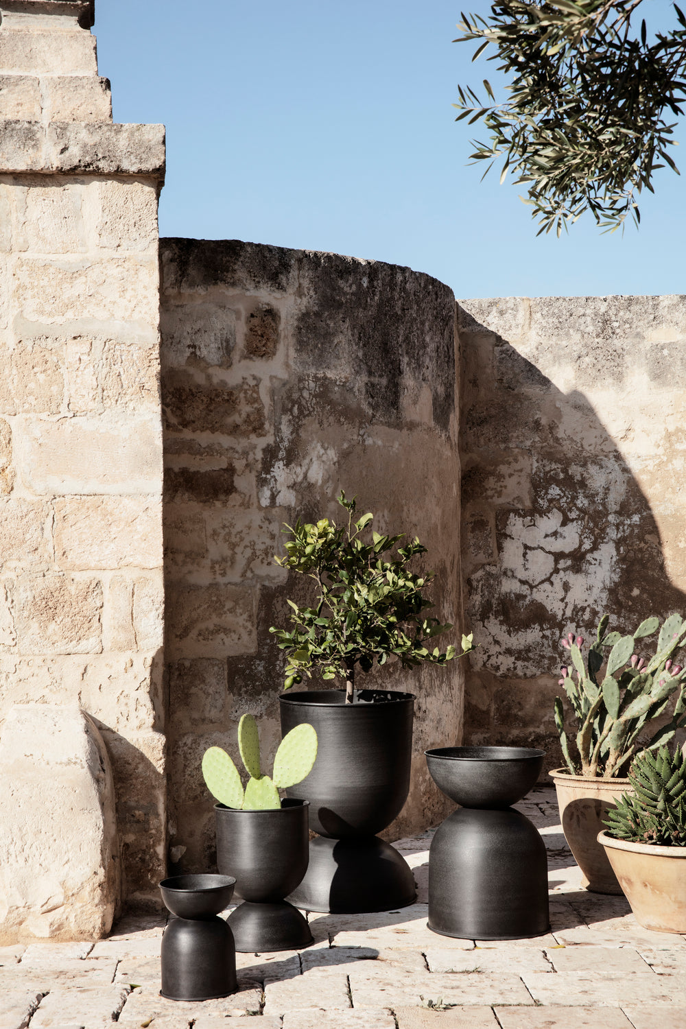 Hourglass Pots, Various Sizes, Black / Dark Grey by ferm LIVING, holding plants on a stone terrace