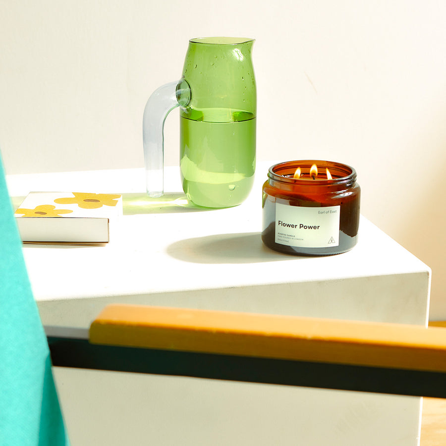 Flower Power, Soy Wax Candle, 500ml [17.5oz] by Earl of East, lit beside a green glass vase in sunlight