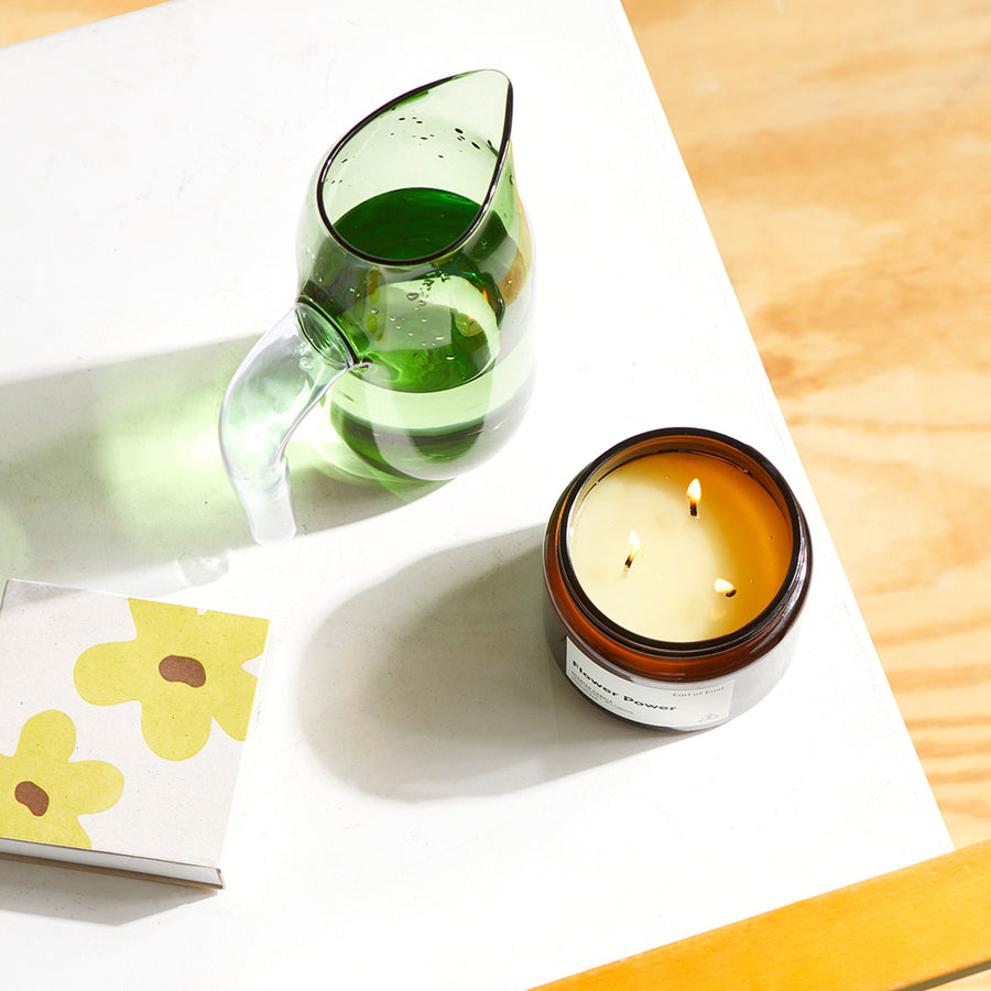 Flower Power, Soy Wax Candle, 500ml [17.5oz] by Earl of East, lit beside green glassware in sunlight