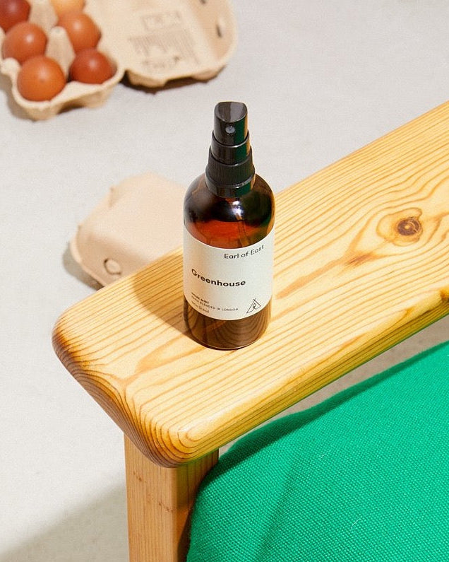 Greenhouse Home Mist, 100ml by Earl of East, on a wooden table beside a green chair