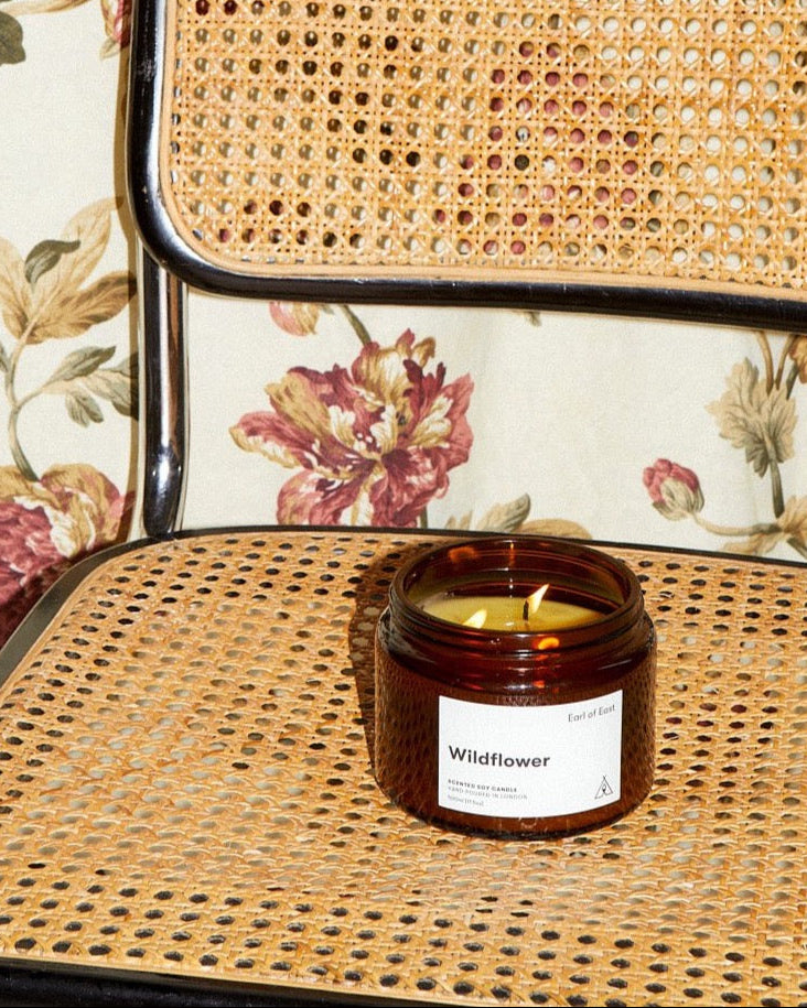 Wildflower Large Scented Candle, 500ml by Earl of East, lit on a cane chair against floral fabric