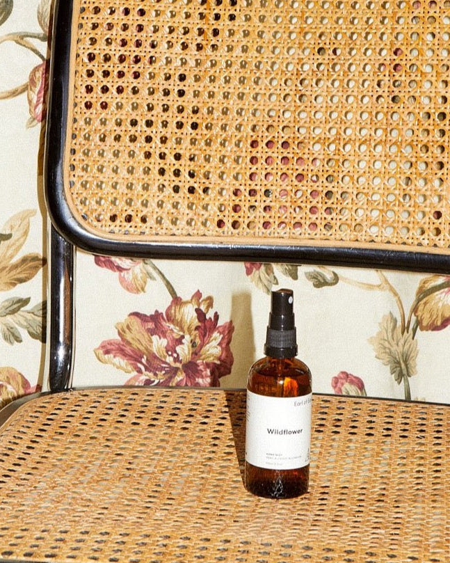 Wildflower Home Mist, 100ml by Earl of East, on a cane chair against floral fabric