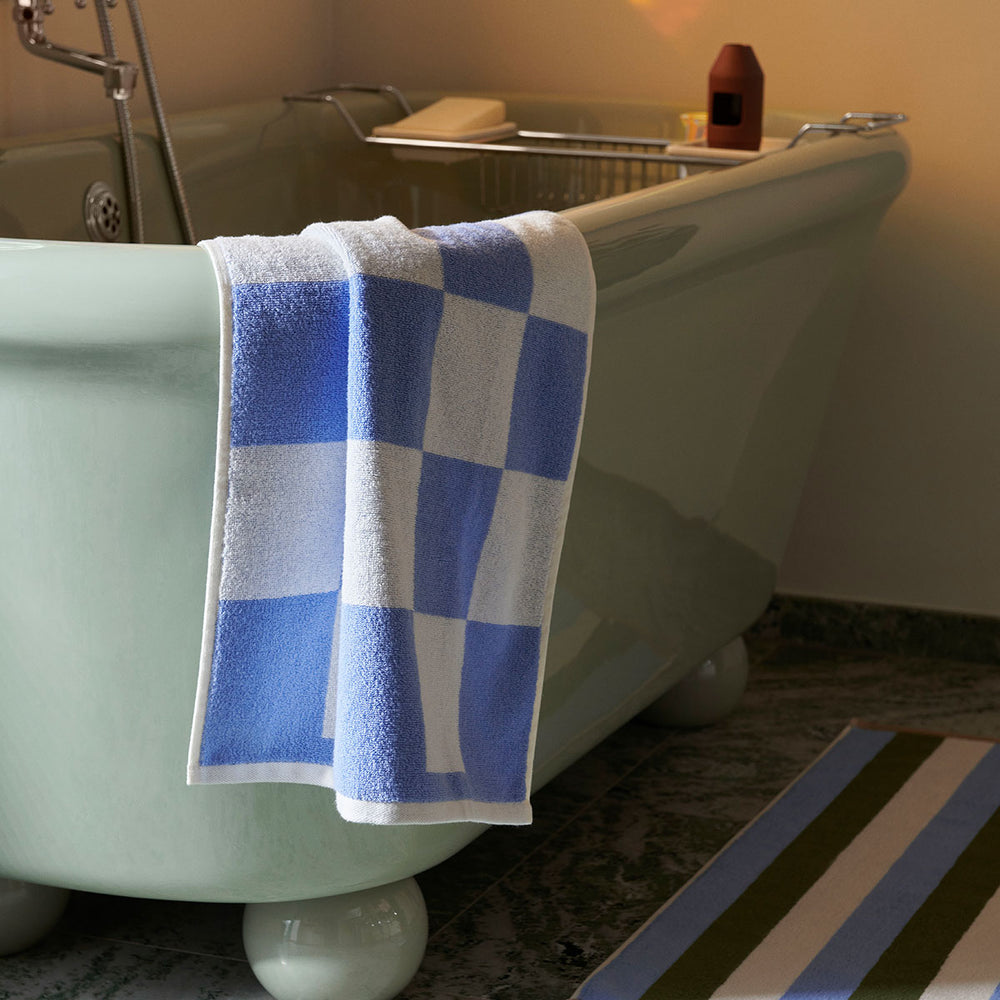 Check Bath Mat, Sky Blue by HAY, hanging on a bathtub edge